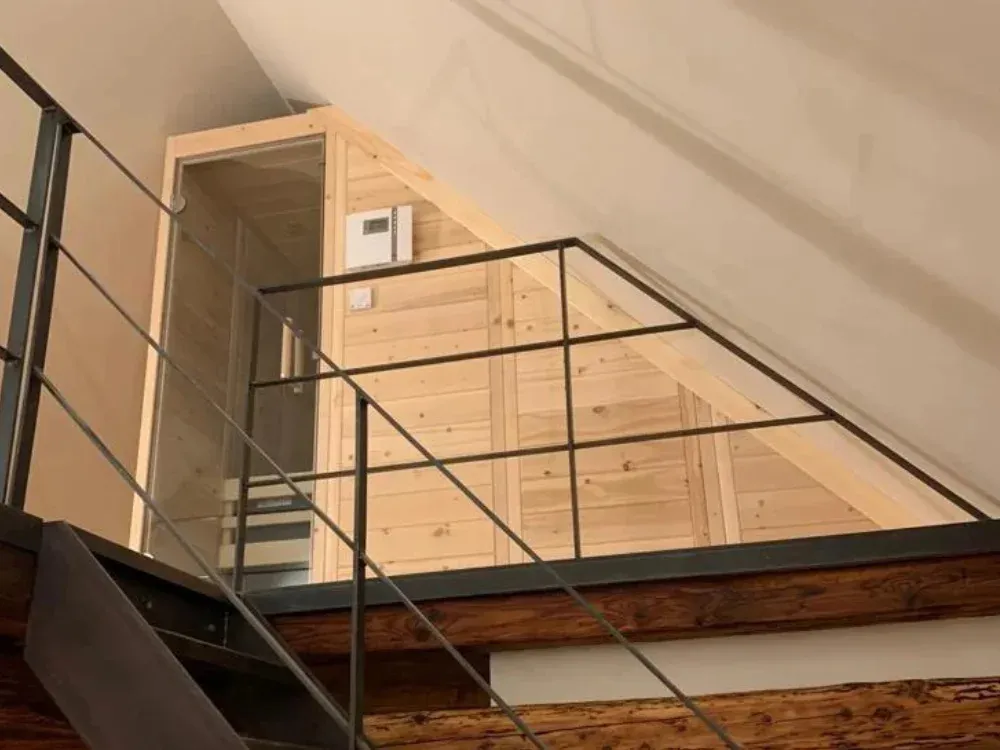 Maßanfertigung unter einer Dachschräge: die Sauna folgt mit ihrer schrägen Oberkante genau der Dachneigung, davor das Geländer einer offenen Treppe.